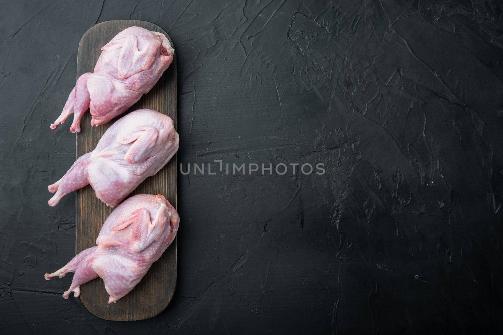 Raw uncooked quails set, top view, on black textured background with copy space