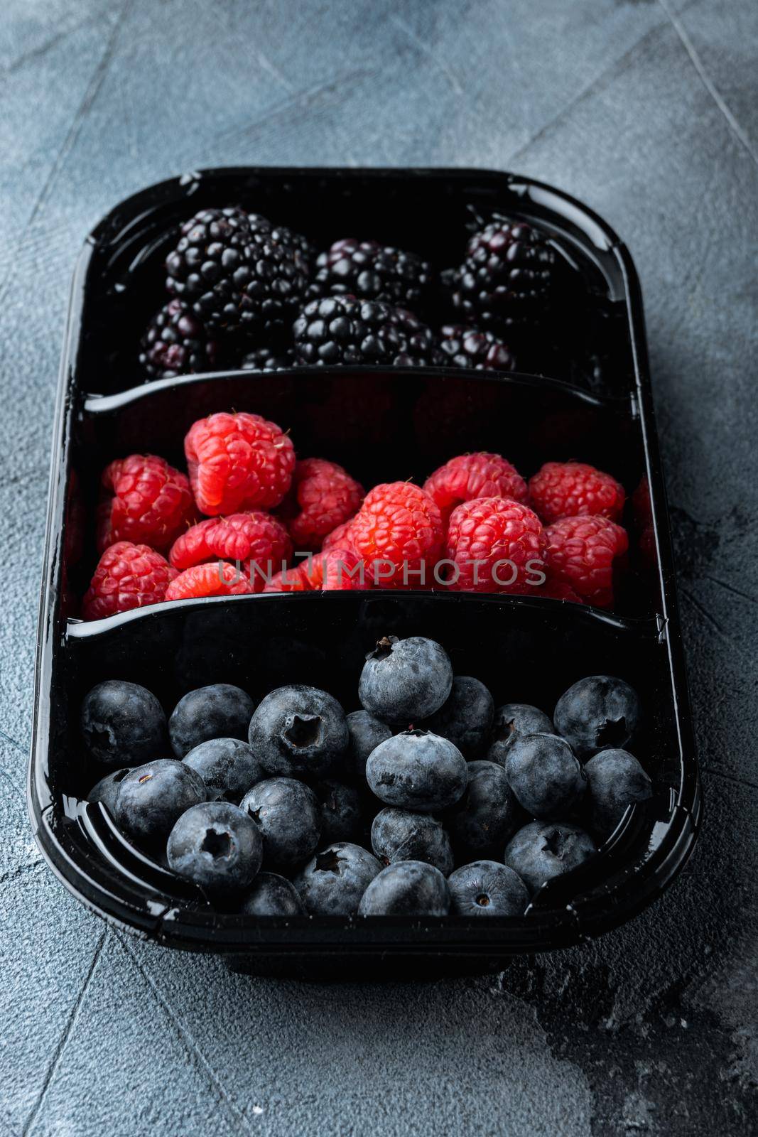 Tray with ripe organic blueberries, raspberry, blackberry, on grey background