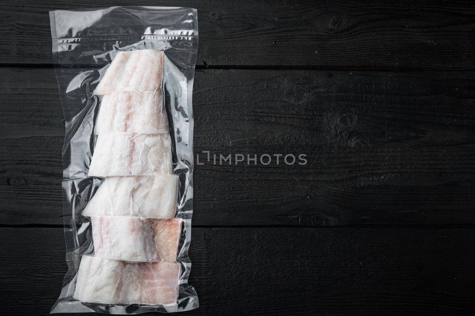 Raw haddock fish skinless plastic vacuum packaged, on black wooden background, top view with copy space for text