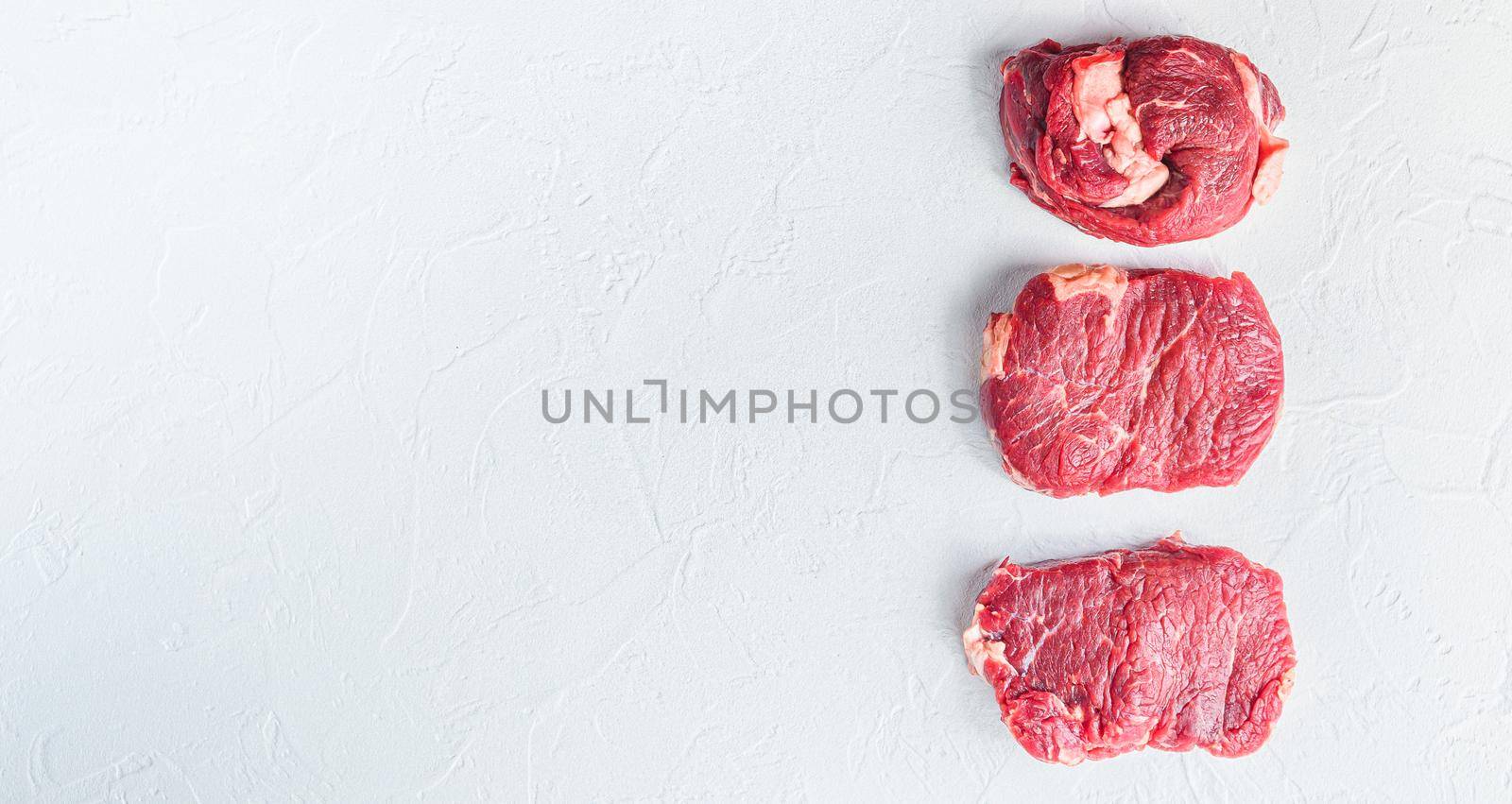 A set of different types of raw beef steaks:top blade, rump, chuck eye roll over white concrete background top view big size banner space for text