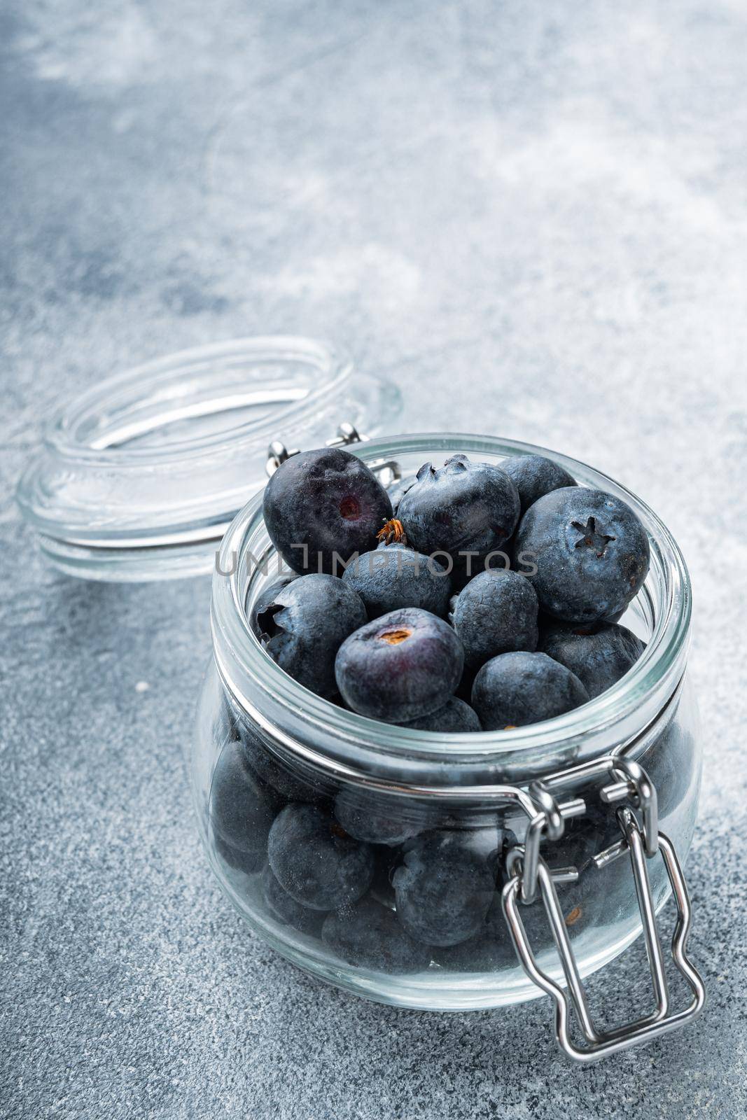 Ripe blueberry in glass jar, on textured background.