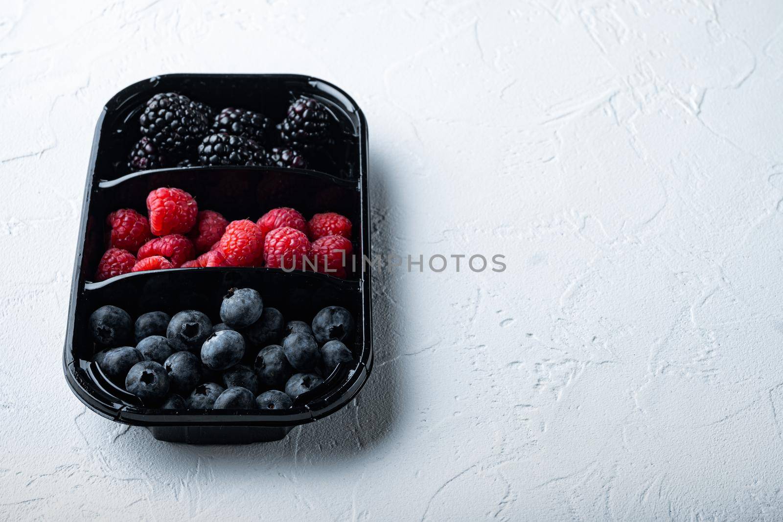 Fresh berries packed in tray, blueberries, raspberry and blackberry with space for text, on white background