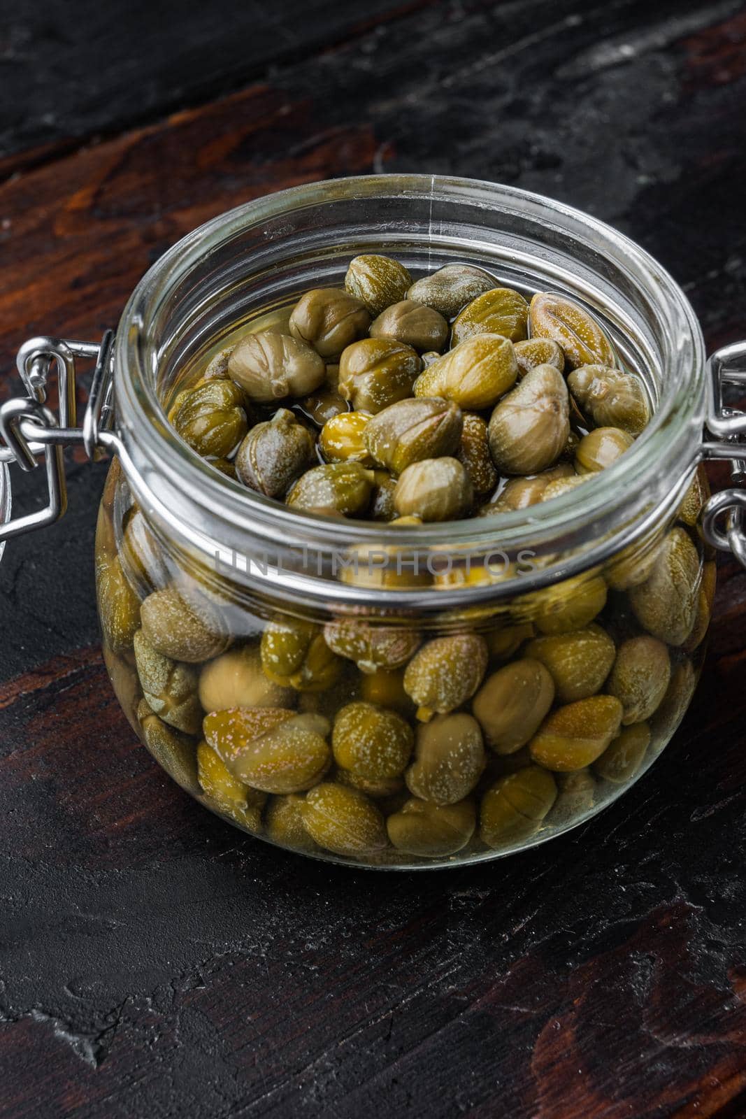 Baby capers in marinate glass jar, on dark wooden background