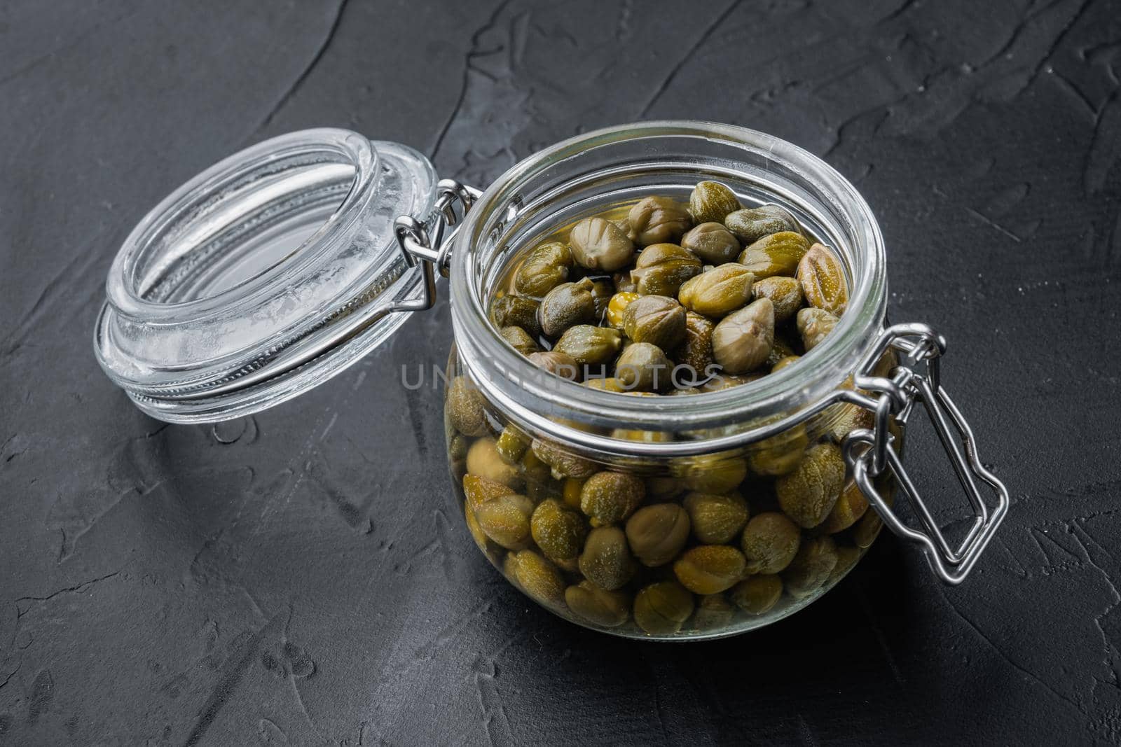 Baby capers in glas jar, on black background