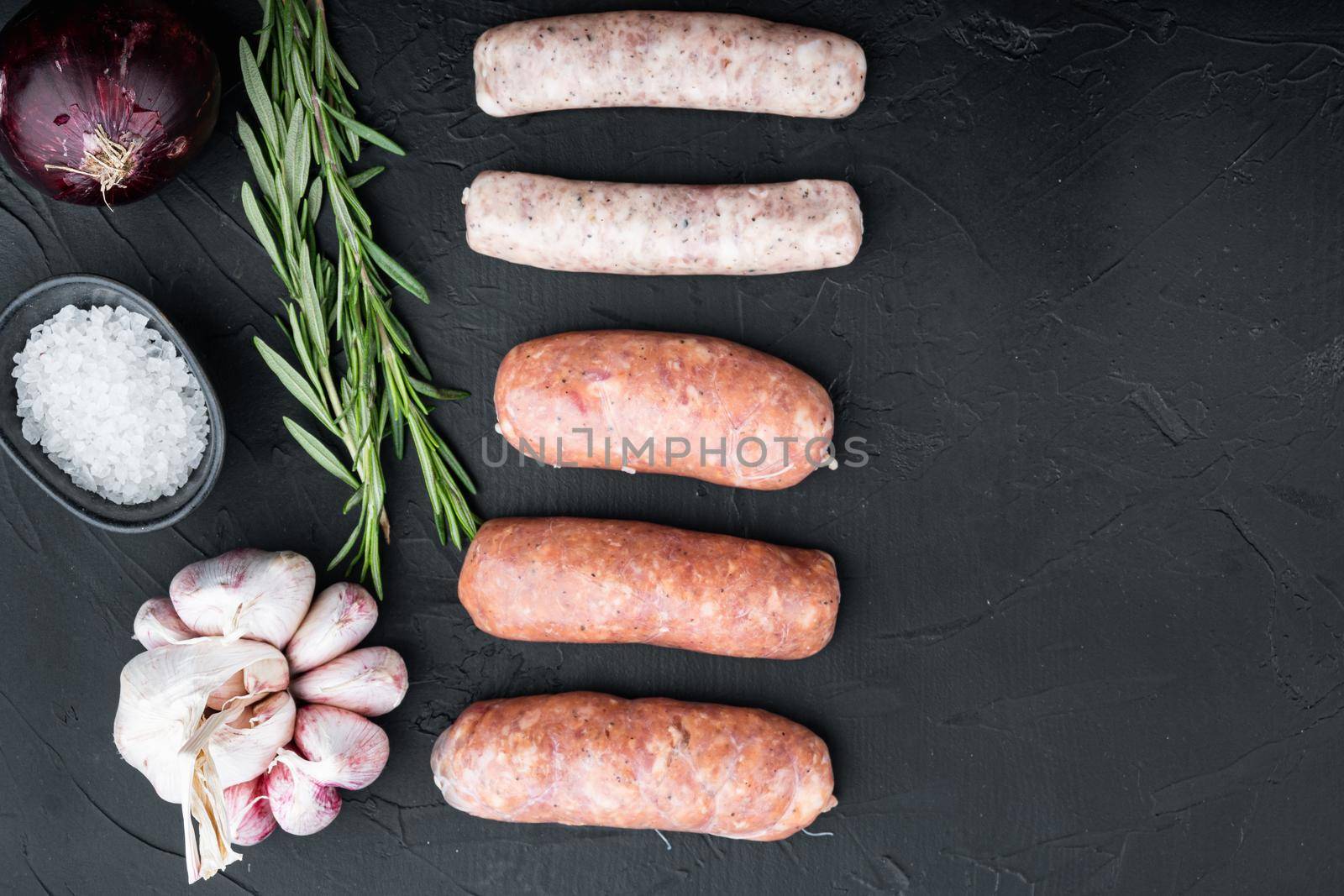 Fresh raw pork, beef and chicken sausages, top view, on black background.