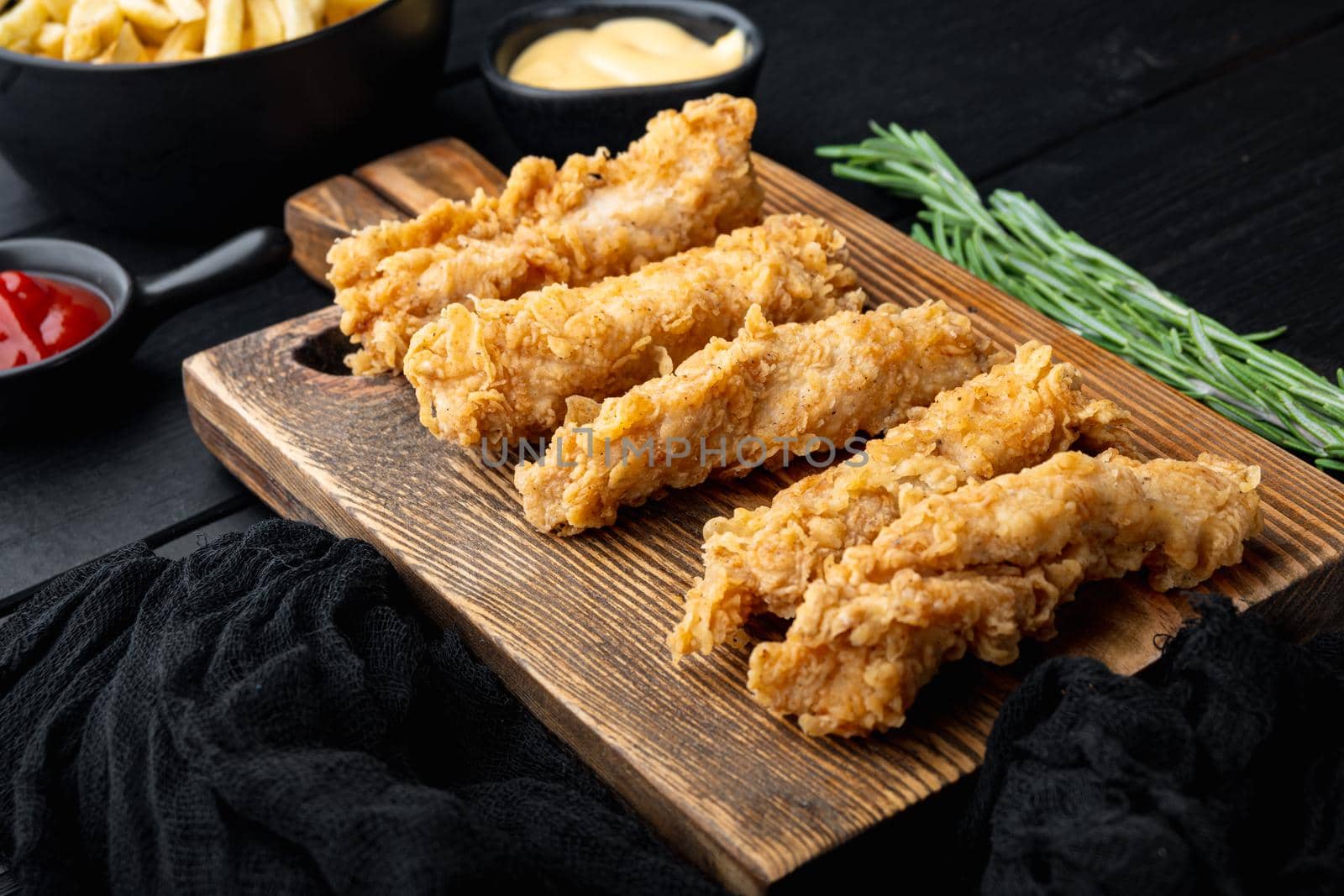 Crispy chicken tenders cuts on black wooden background.