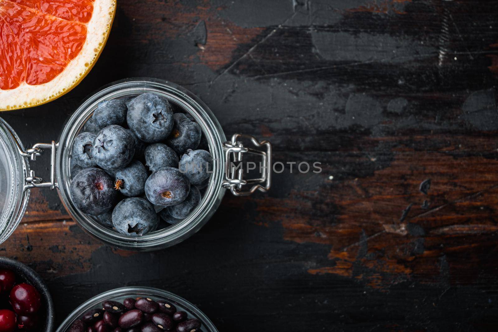 Ripe blueberry in glass jar, flat lay on dark wooden background, with space for text.