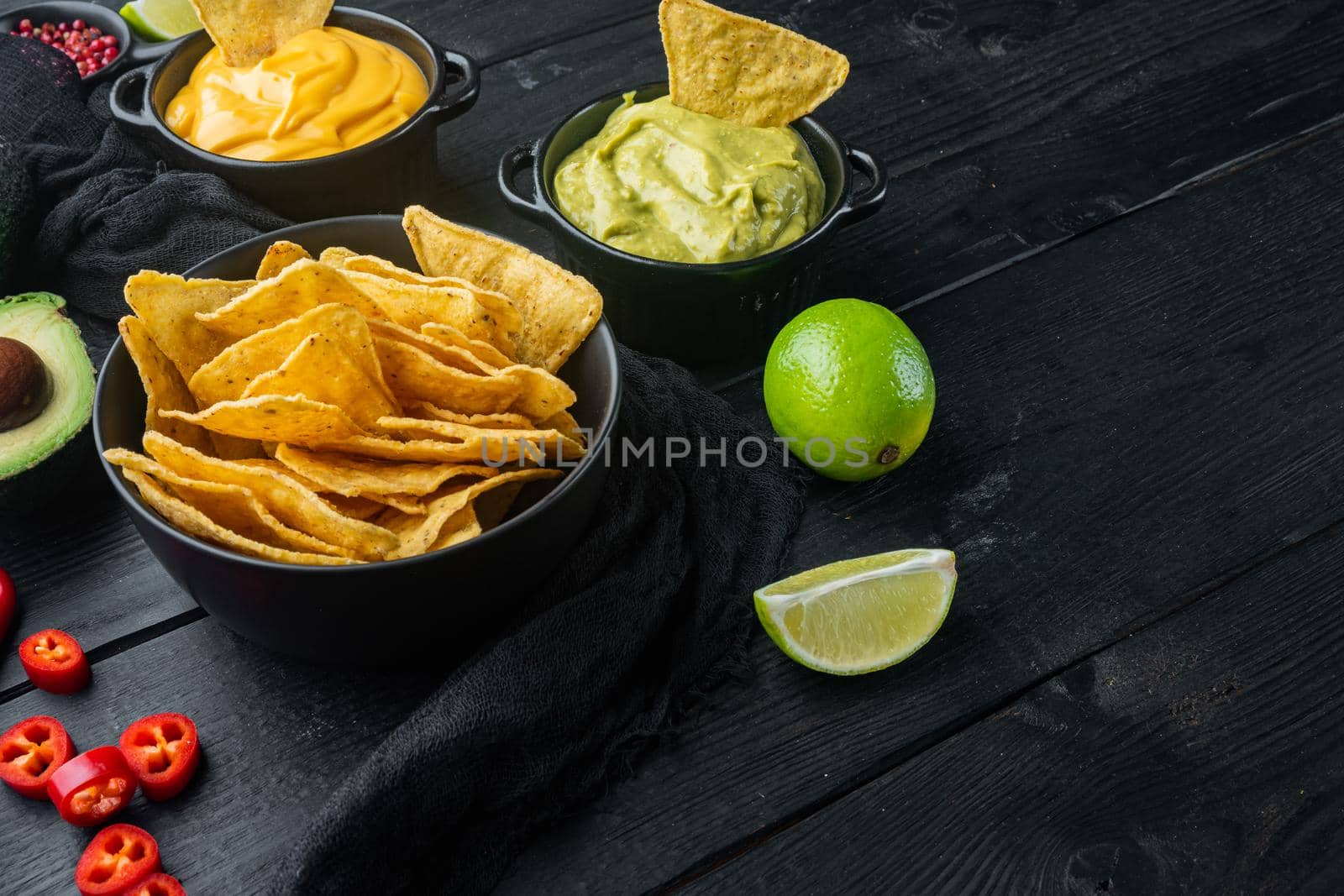 Triangular yellow corn tortilla chip with sauces, on black wooden background with copy space for text