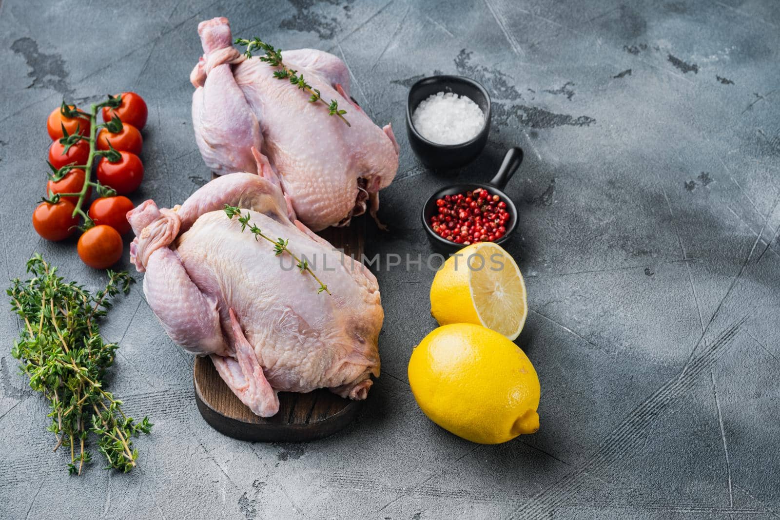 Raw organic uncooked whole chicken meat with herbs and ingredients, on gray background with copy space for text