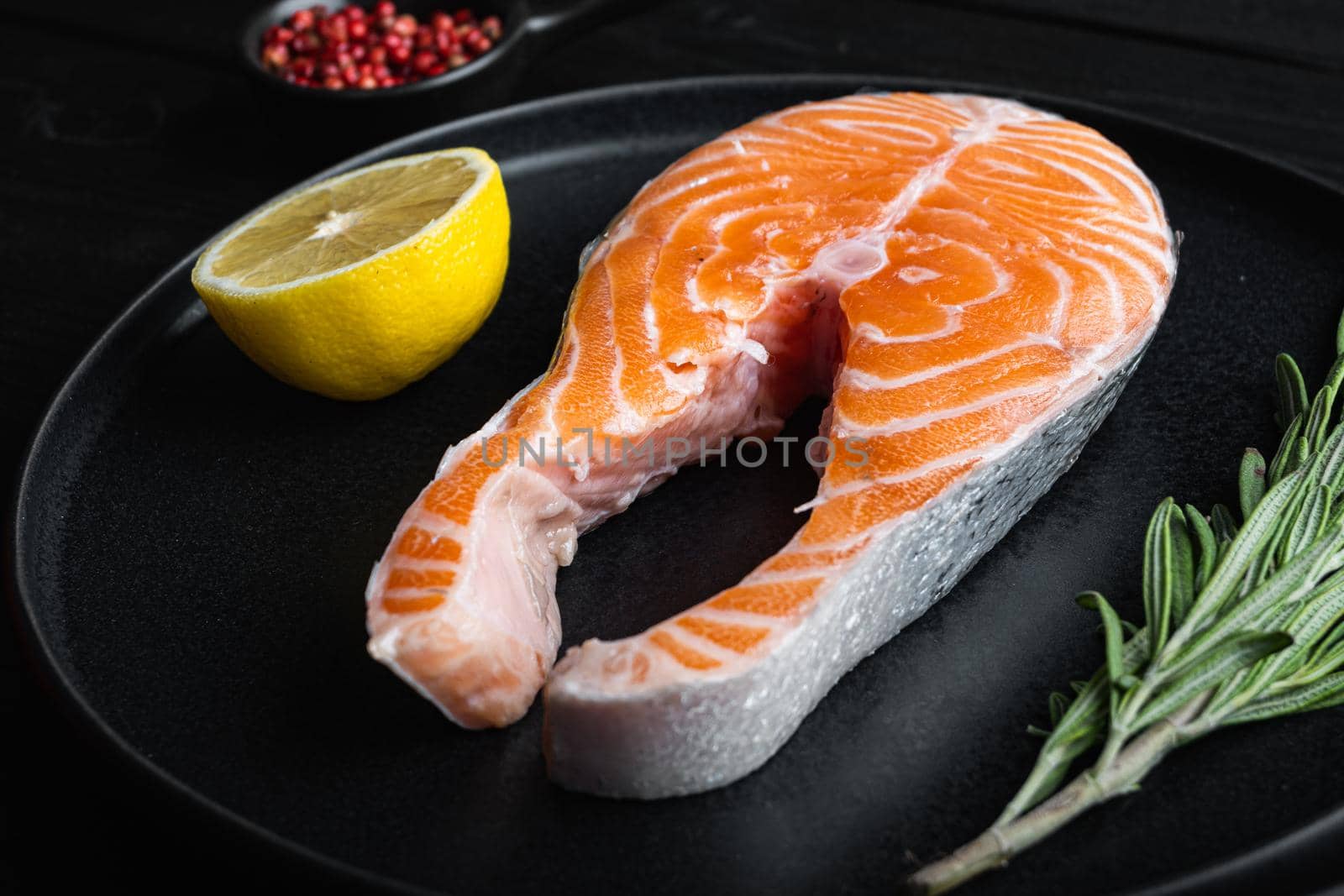 Slice of red fish salmon with herbs, on black wooden surface.