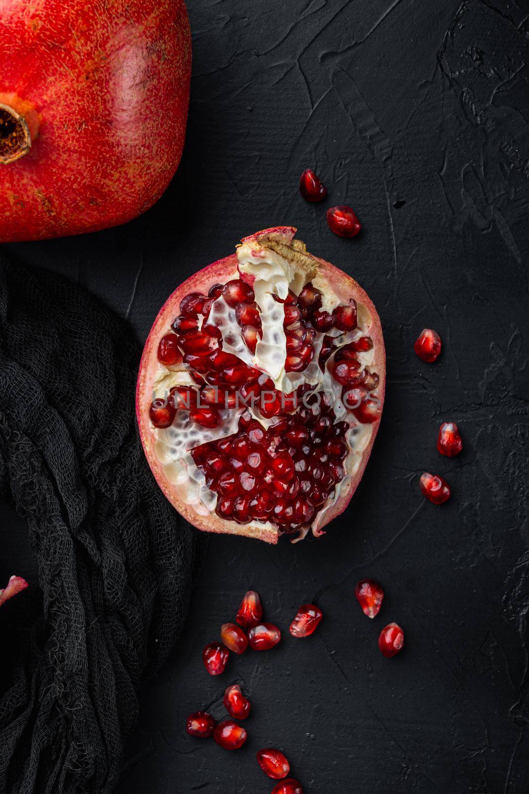 Ripe pomegranate with juicy seeds, on black textured background, top view