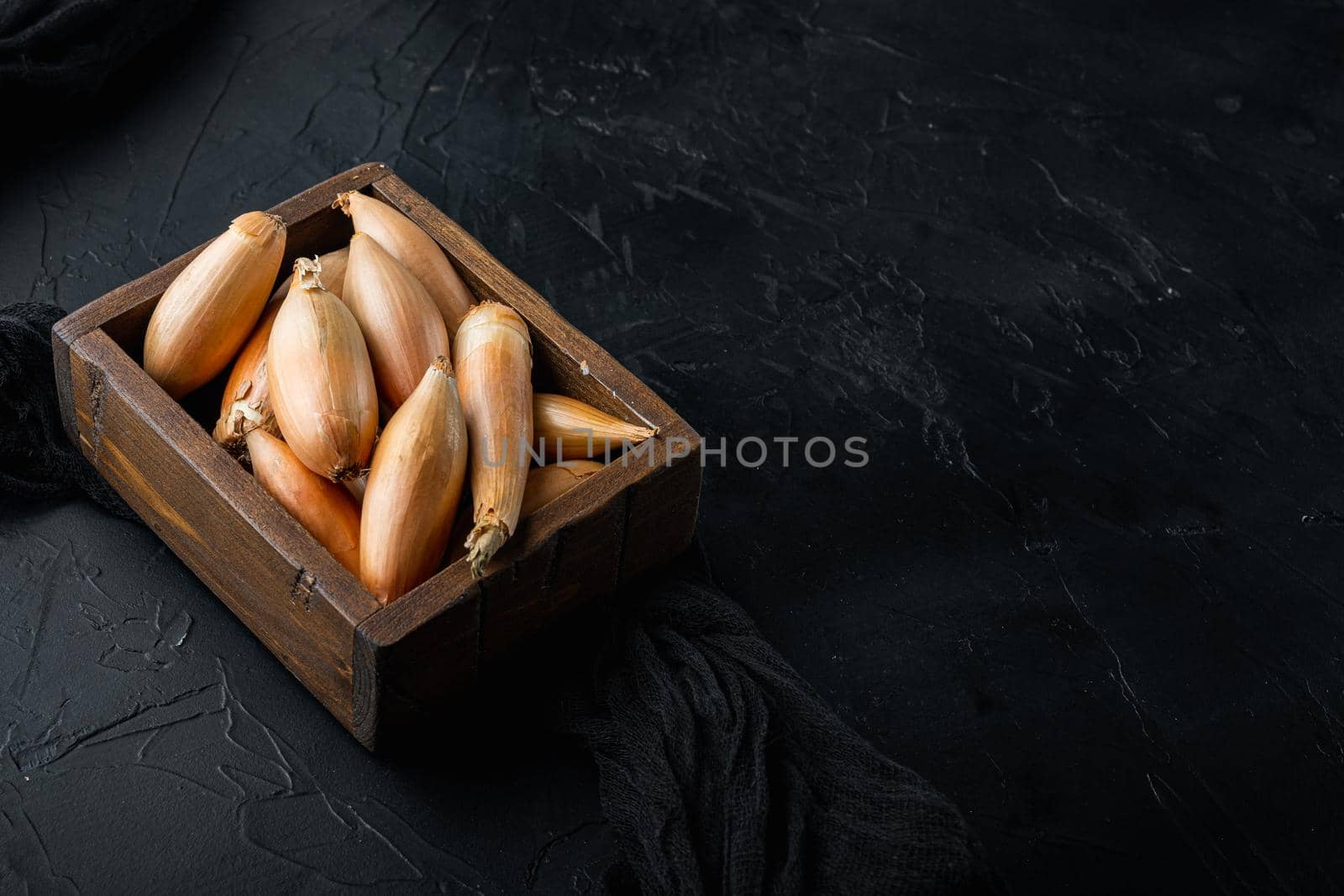Raw whole baby shallot onion, on black textured background with space for text