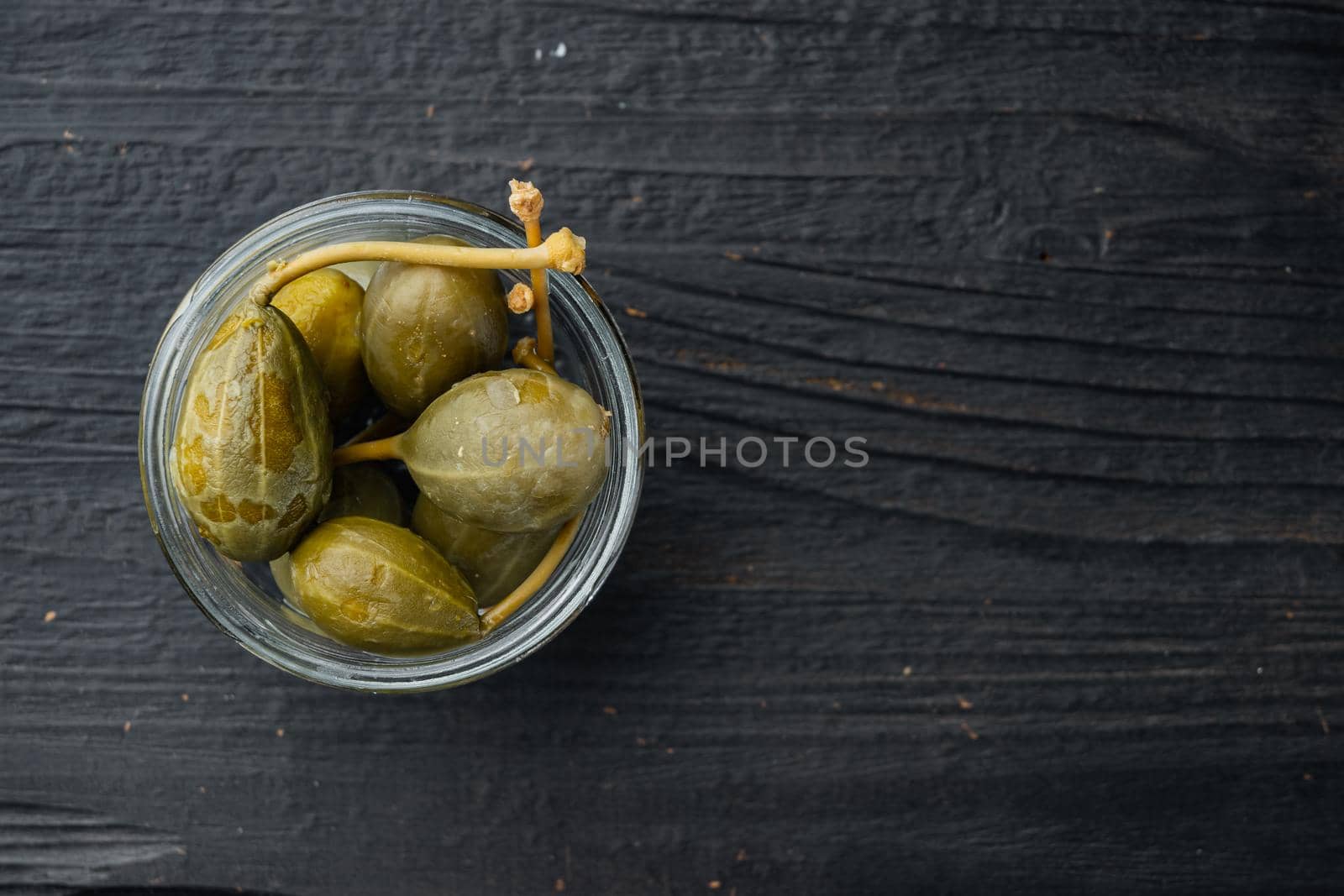 Organic pickled, canned capers, on black wooden background, top view with copy space for text