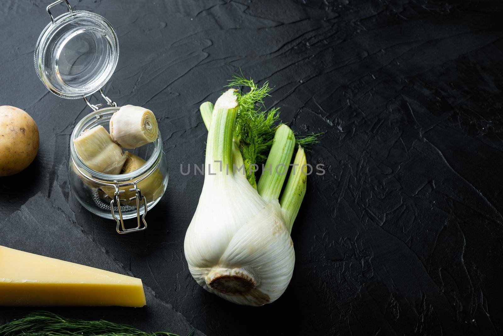 Fennel and artichoke with parmesan raw ingredient, on black textured background with space for text
