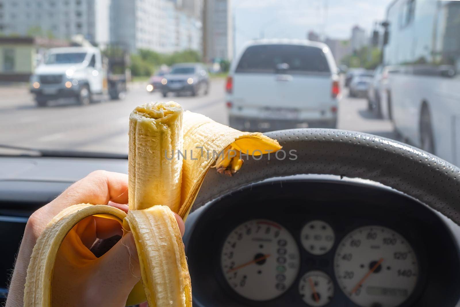 Food, banana in the hand of a driver driving a car that is driving on a city street among city traffic