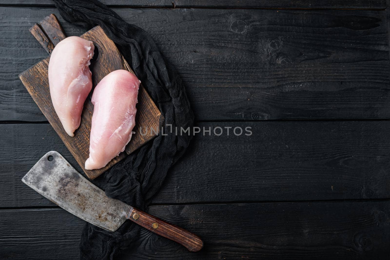 Chicken raw fillets with butcher knife on black wooden table, flat lay with space for text