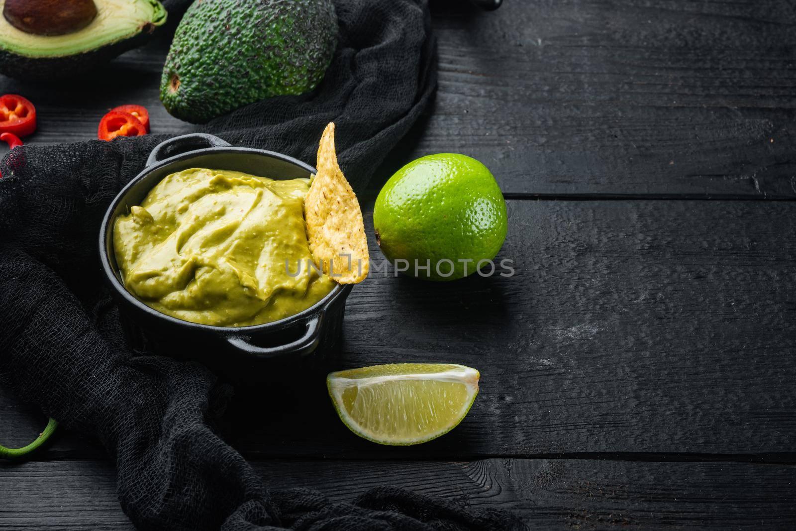 Nachos corn tortilla chip with avocado dip or guacamole in bowl, on black wooden background with copy space for text