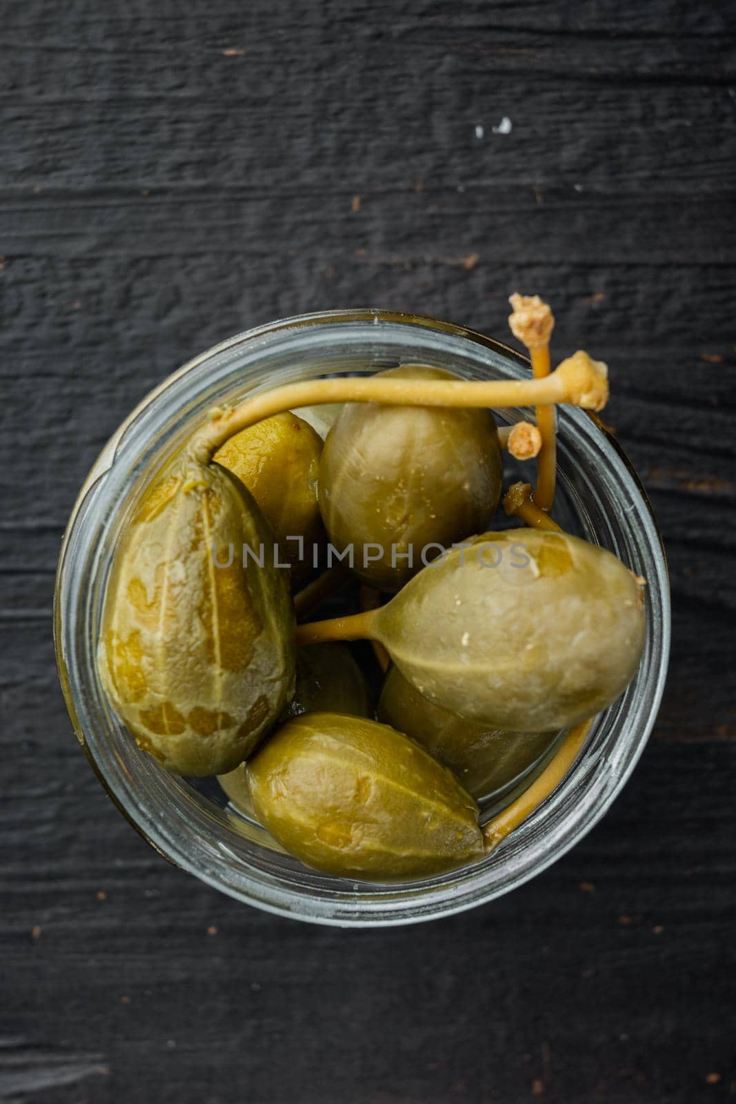 Capers, marinated in oil, on black wooden background, flat lay
