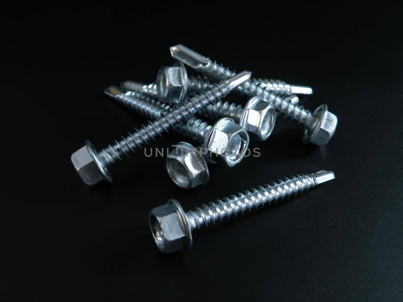 small amount Self-tapping screws galvanized with a semicircular head and a hex head on a black background.