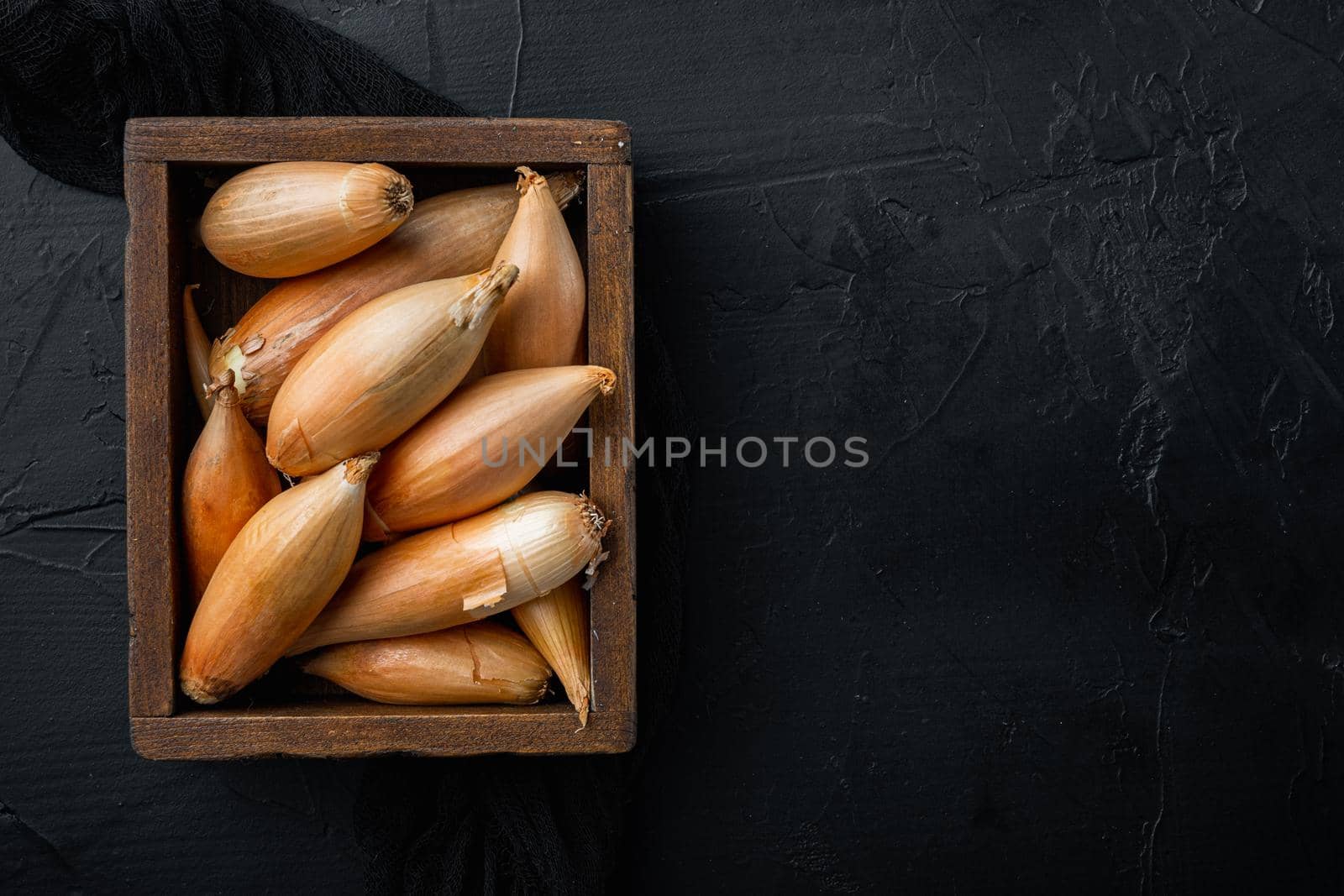 Raw whole baby shallot onion, on black textured background, flat lay with space for text