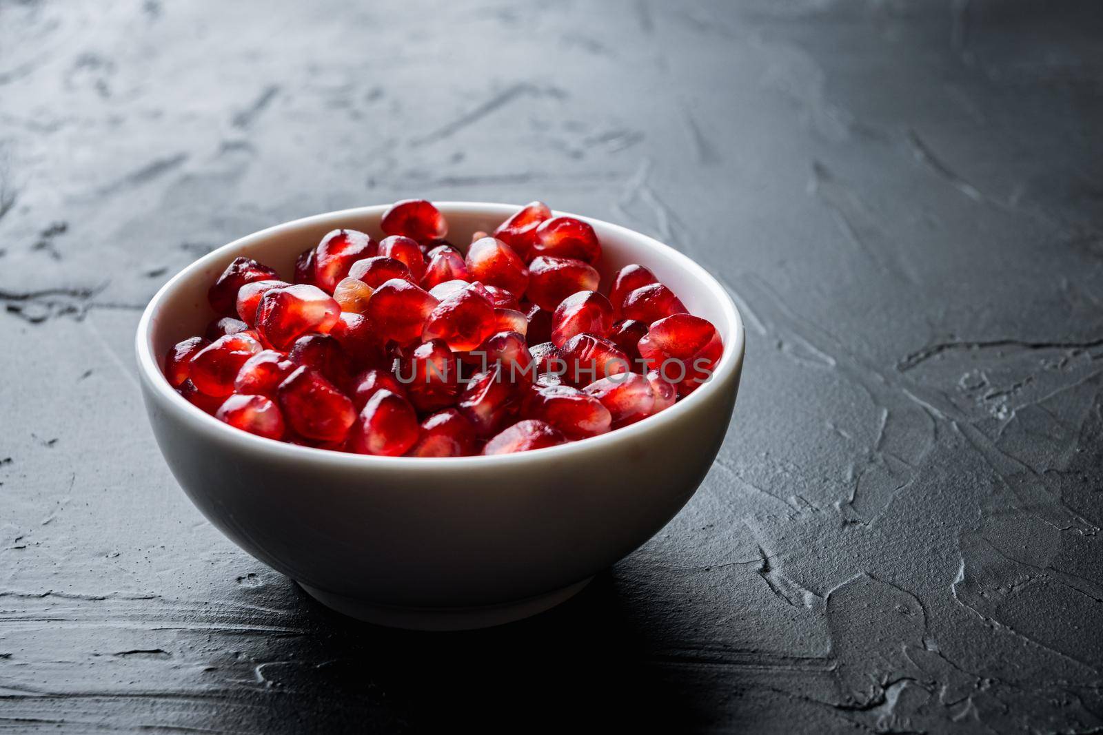 Ripe pomegranate with juicy seeds, on black textured background with space for text