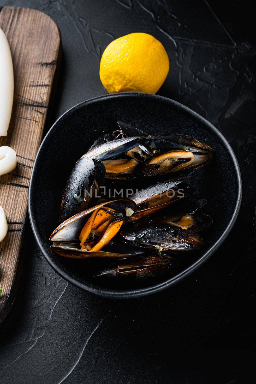 Steamed mussels in black bowl on black concrete surface, flat lay, food photo.