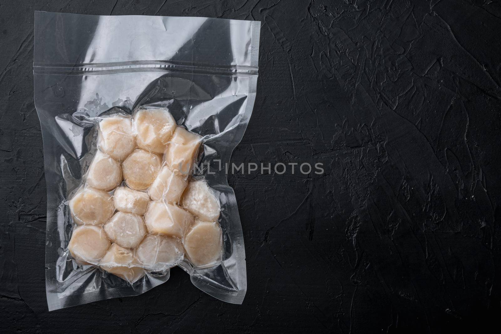 Scallops, in vacuum pack, top view, on black textured background with copy space