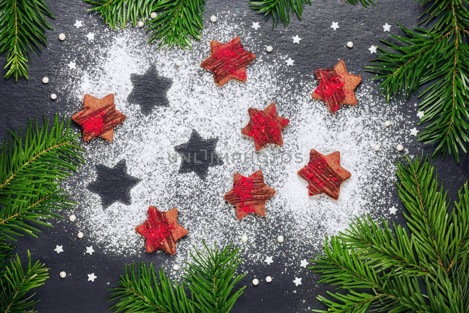 Homemade christmas cookies chocolate stars with raspberry crunches with sugar powder on slate table with pine branches