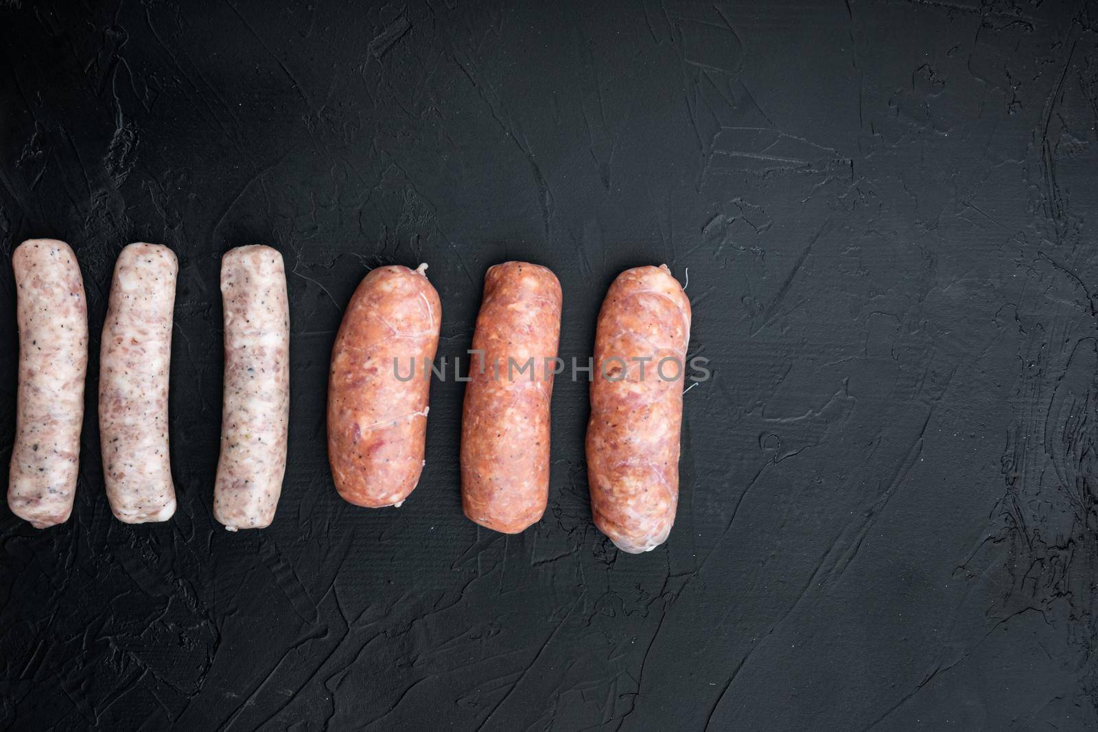 Fresh raw pork, beef and chicken sausages, top view with space for text, on black background.