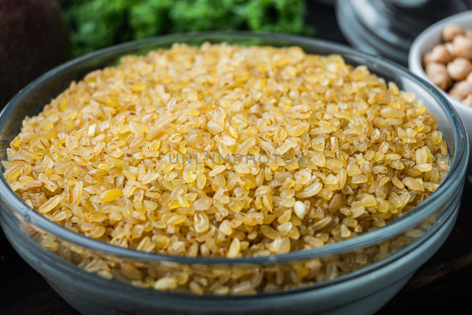 Bulgur grain in bowl on dark wooden background.