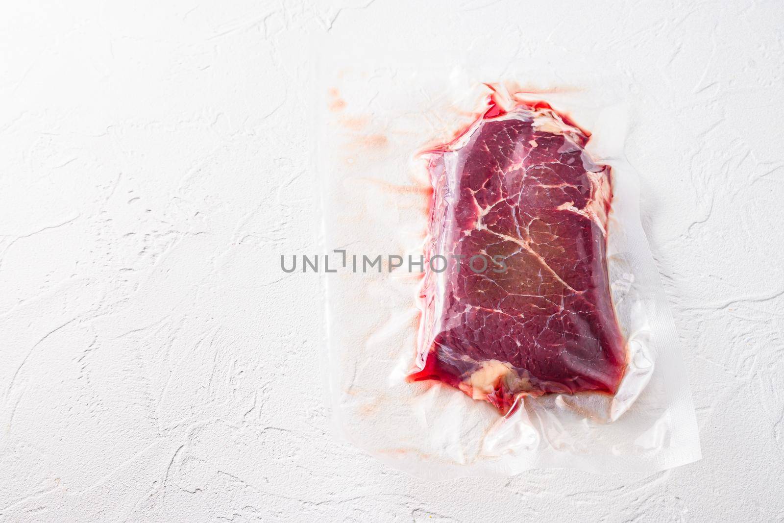 Vacuum packed organic beef meat rump steak on white concrete textured background, top view space for text