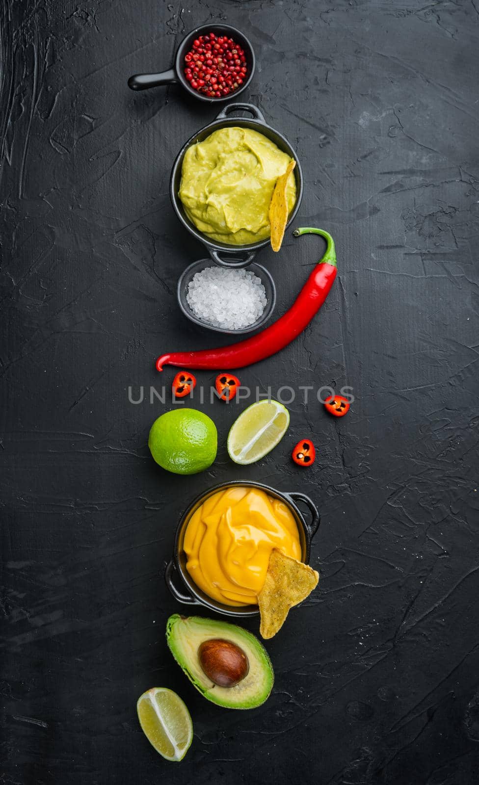 Green guacamole and yellow cheese dip sauce for traditional, Mexican tacos, on black background, top view or flat lay with copy space for text