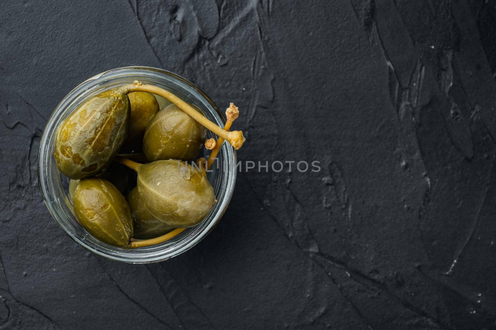 Capers, marinated in oil, on black background, flat lay with copy space for text