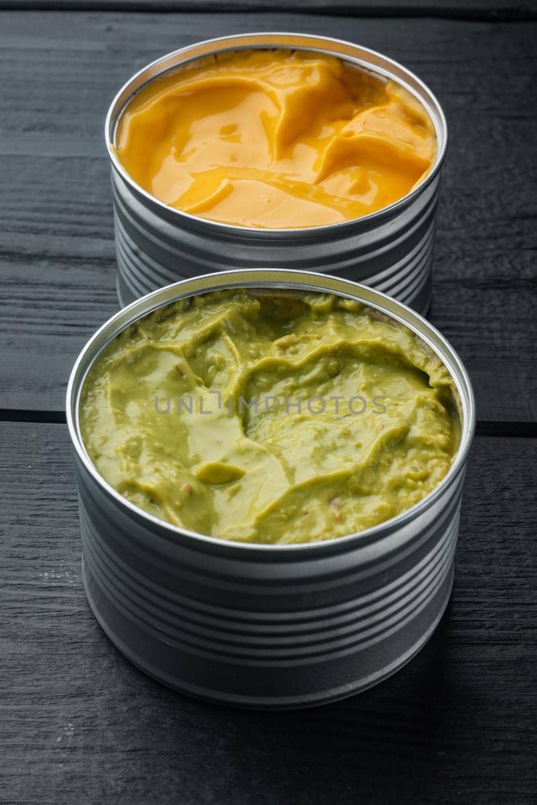 Canned cheese and guacamole sauce in can, on black wooden background
