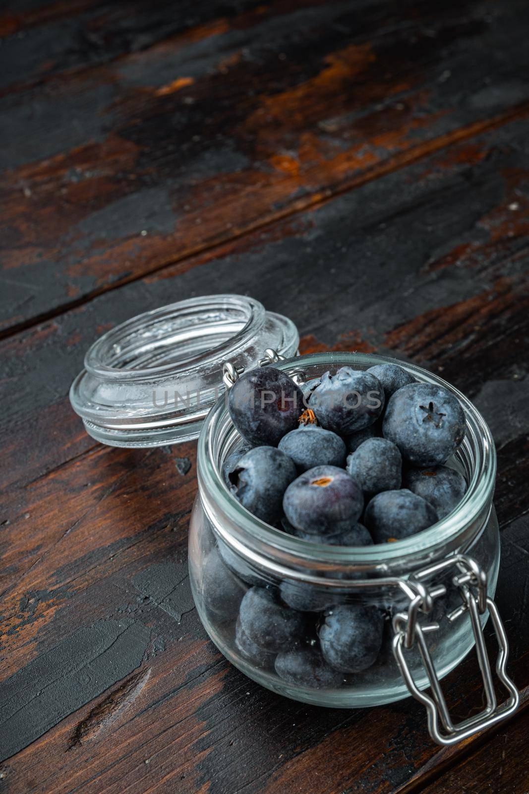 Ripe blueberry in glass jar on old wooden background.