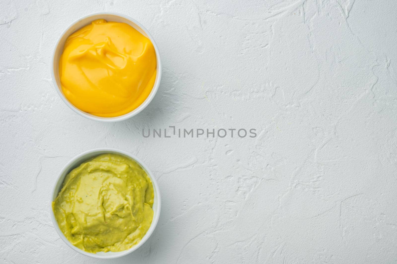 Green guacamole and yellow cheese dip sauce for traditional, Mexican tacos, on white background, top view or flat lay with copy space for text