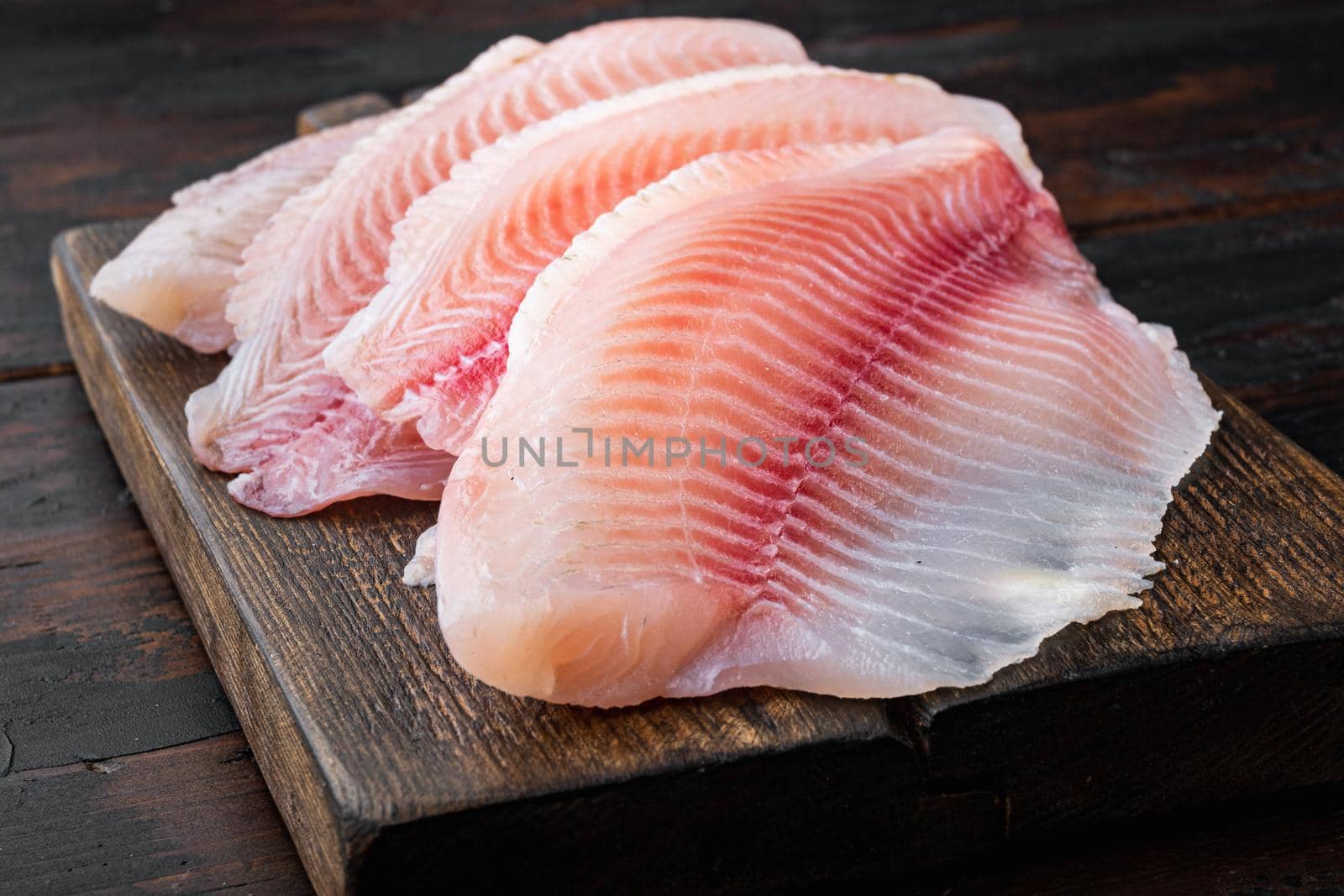 Raw white fish fillet cuts, on dark wooden background