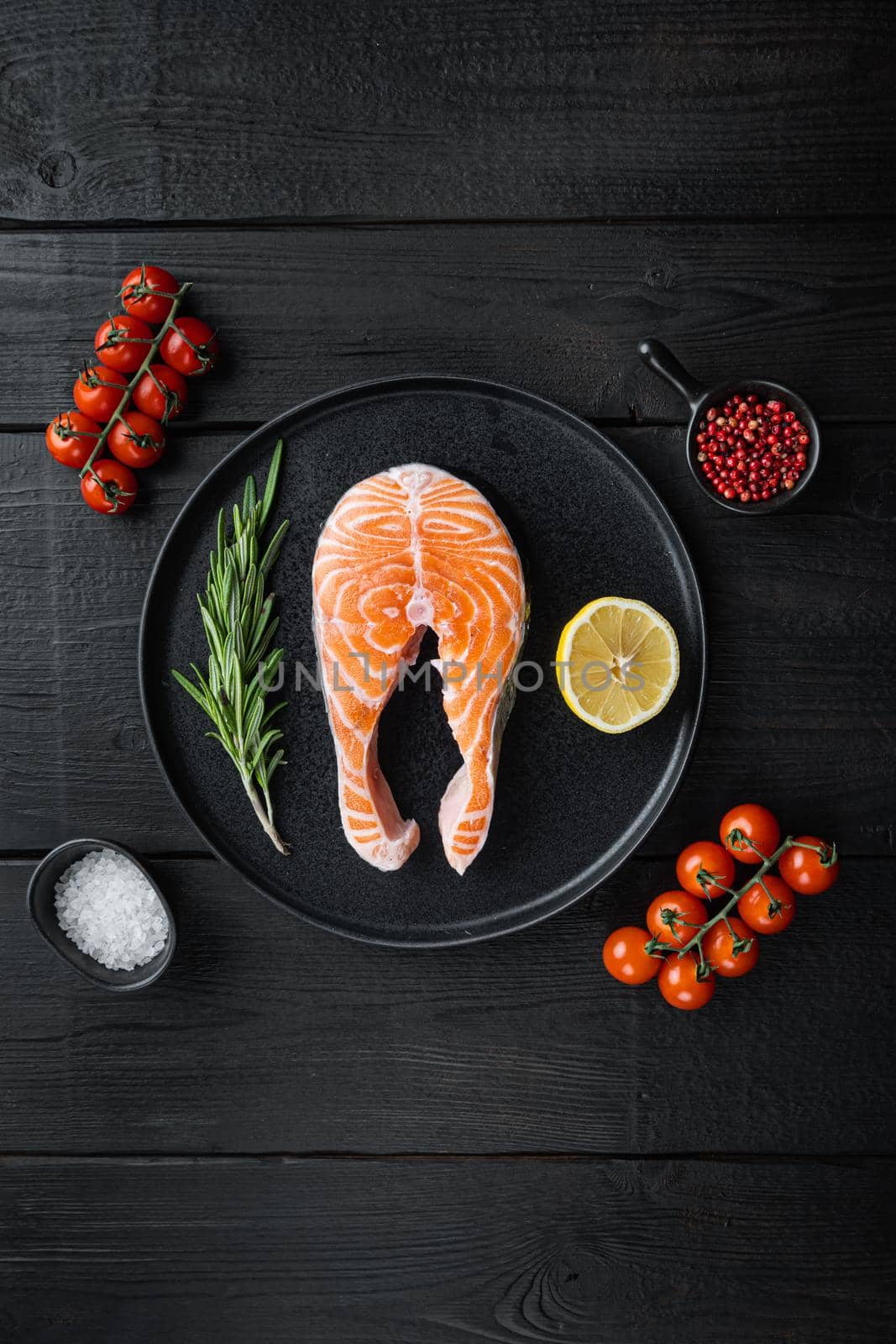 Slice of red fish trout with herbs, on black wooden surface, flat view with space for text.
