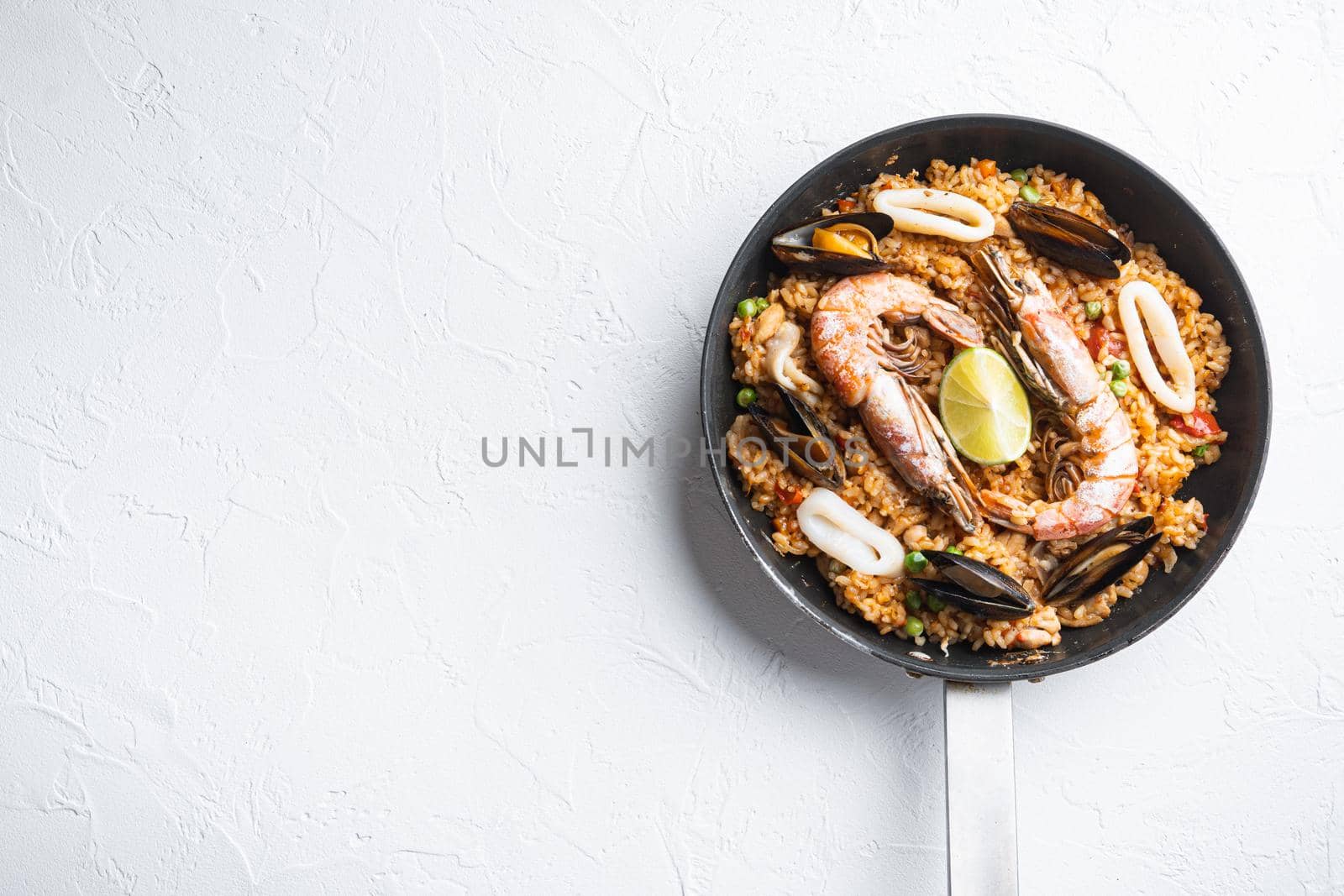 Paella with seafood and chicken on white background, top view with space for text, food photo.