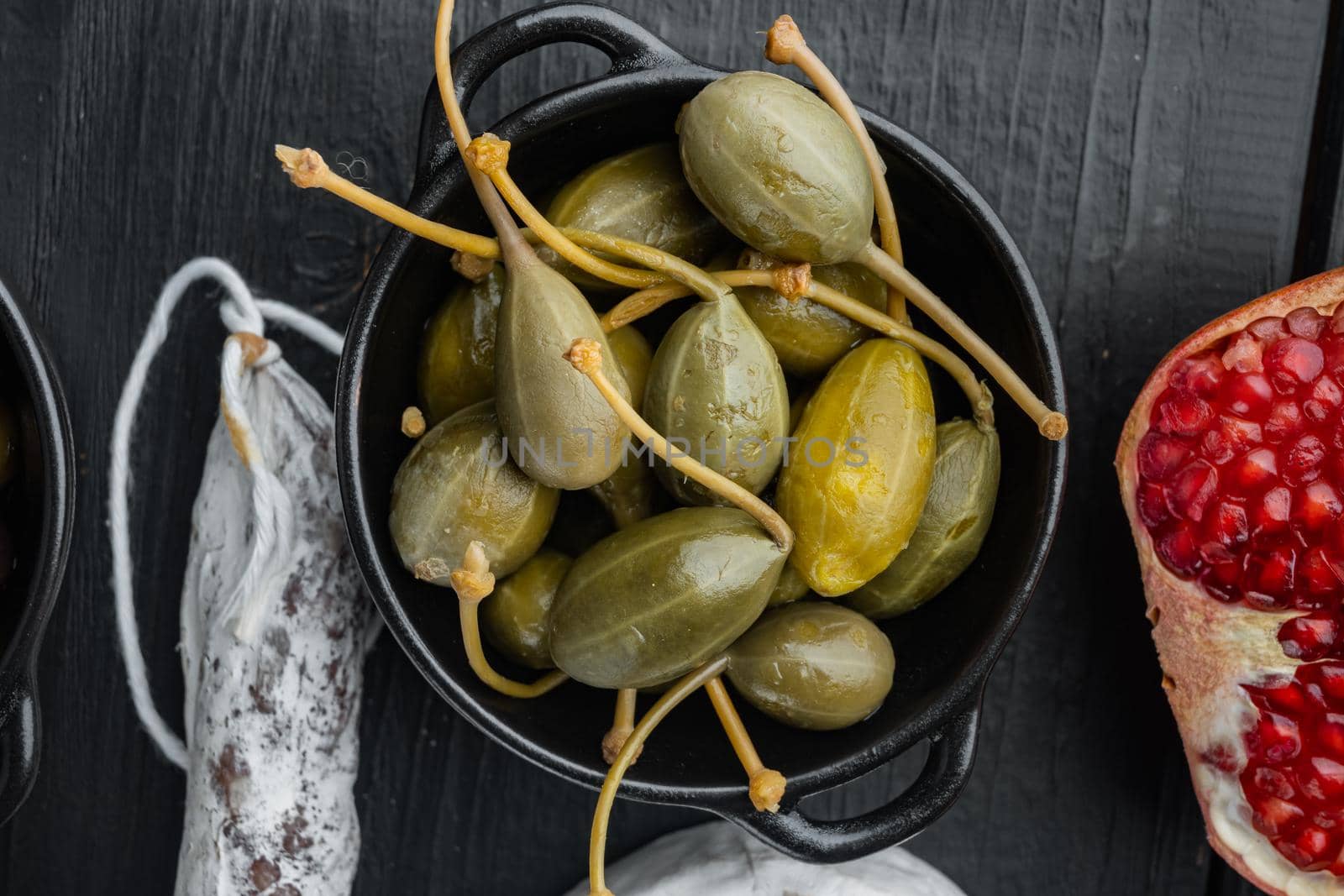 Capers, marinated in oil, on black wooden table, flat lay
