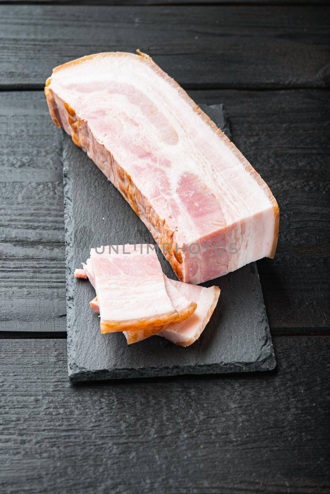 Smoked bacon, whole slab on black wooden table.