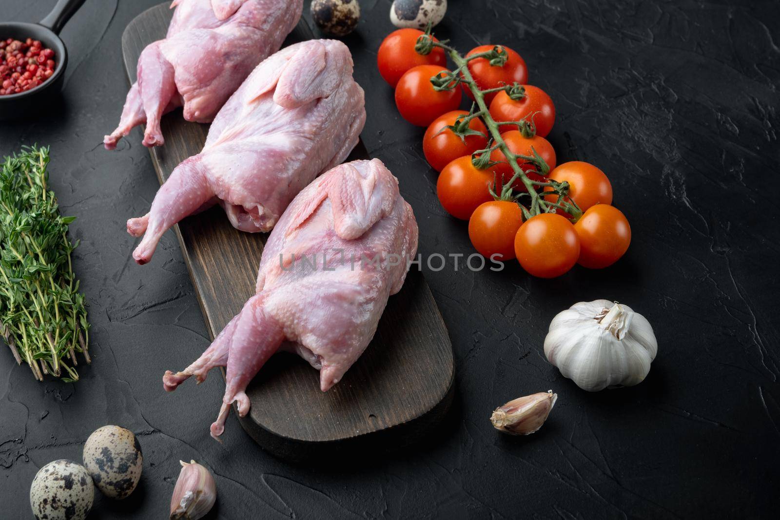 Fresh raw meat quails with herb, on black textured background