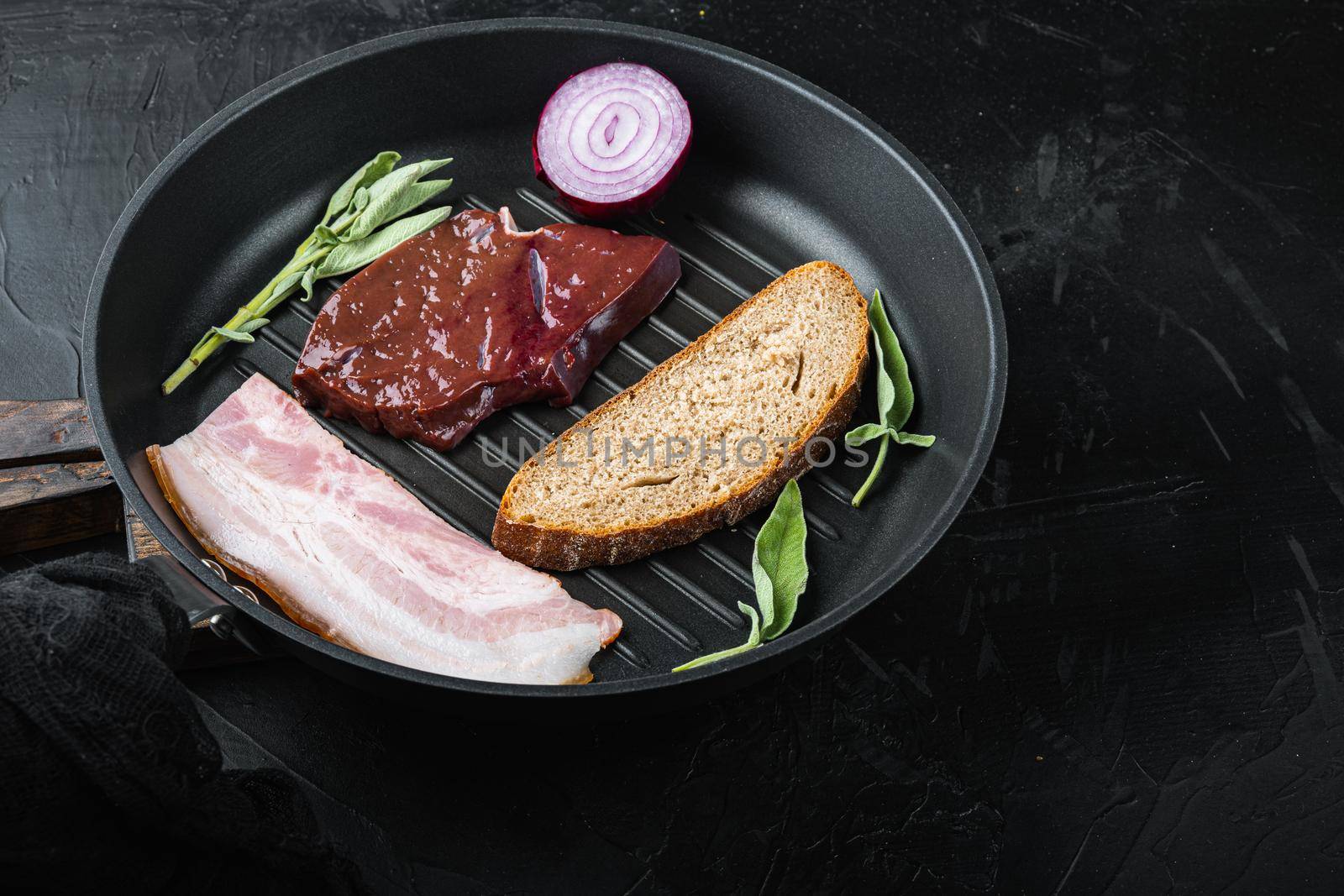 Beef liver sliced with bacon on grill pan on black surface, top view.