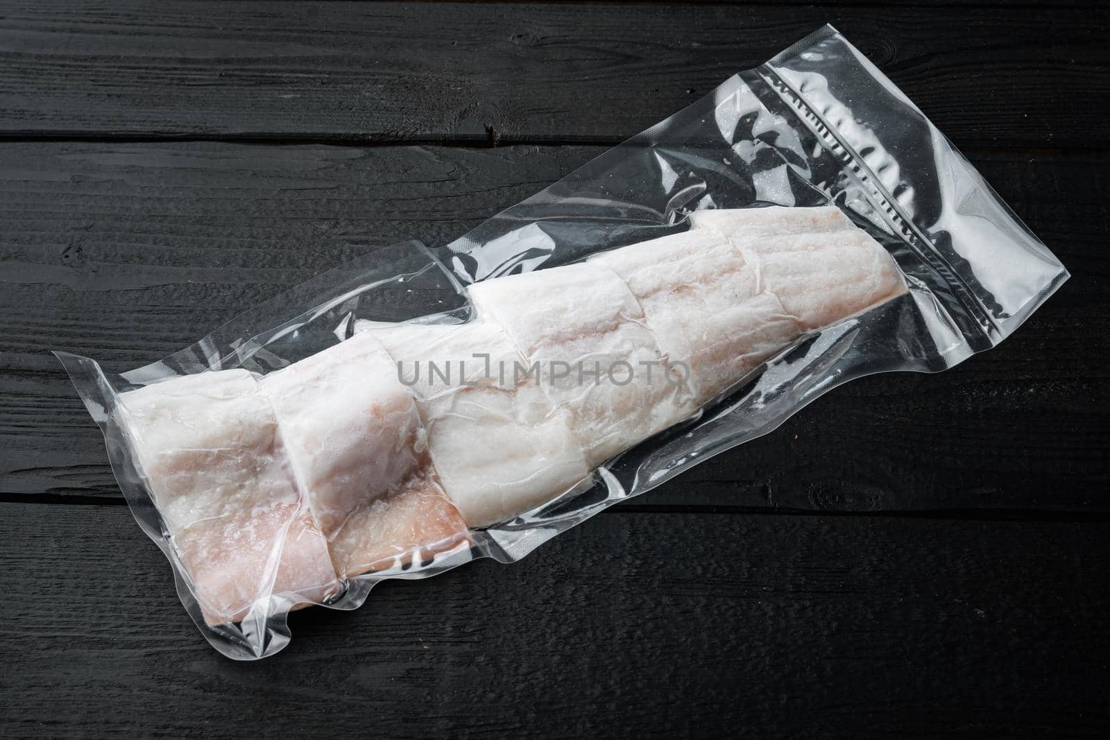 Haddock white fish fillet in plastic market package, on black wooden table with copy space for text