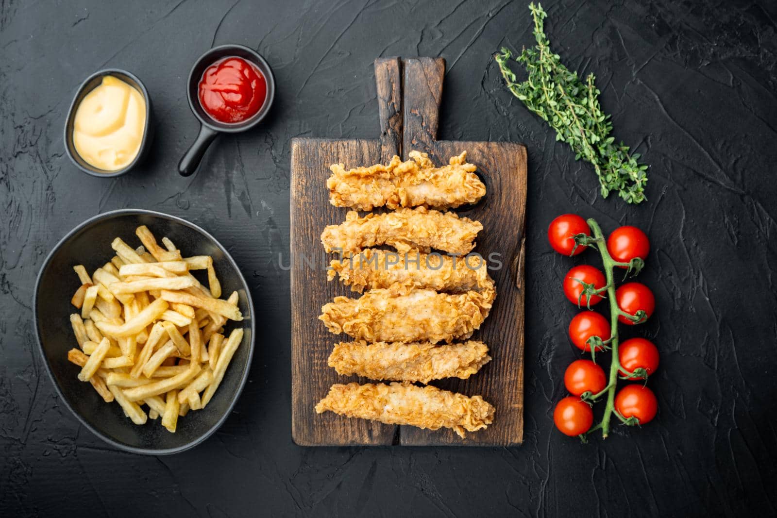 Chicken breaded fillet stripes on black background, flat lay.