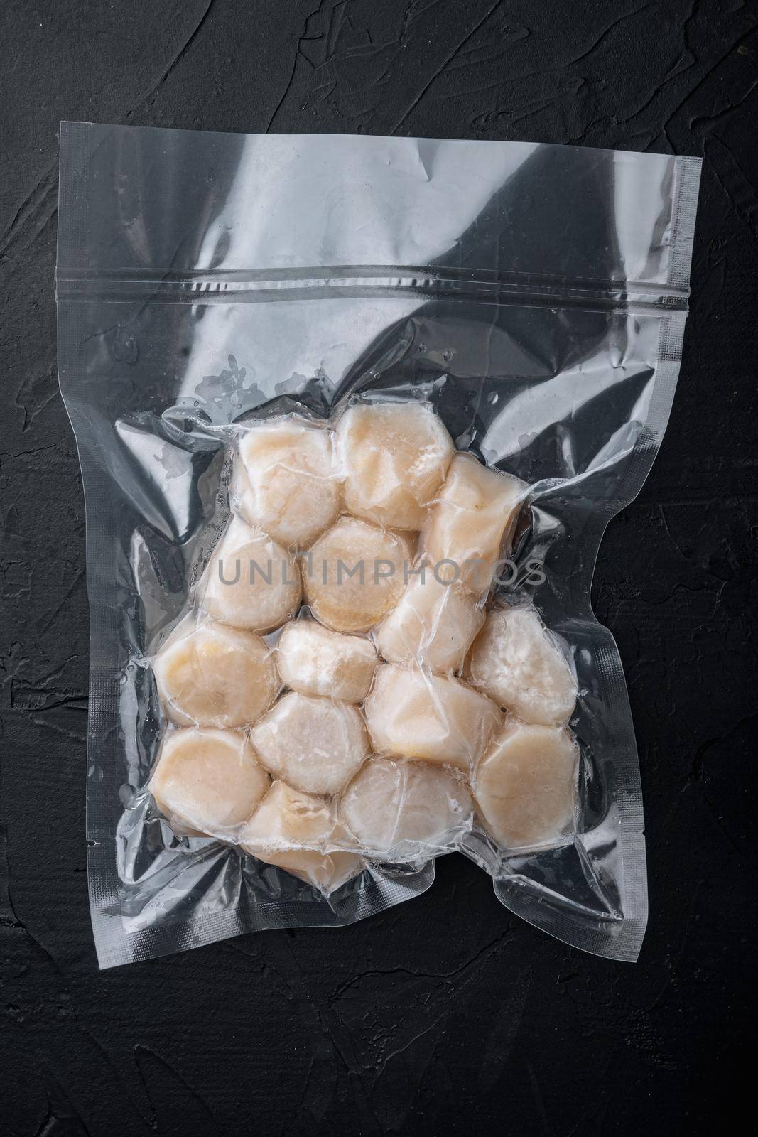 Frozen meat scallops in vacuum package, flat lay, on black textured background