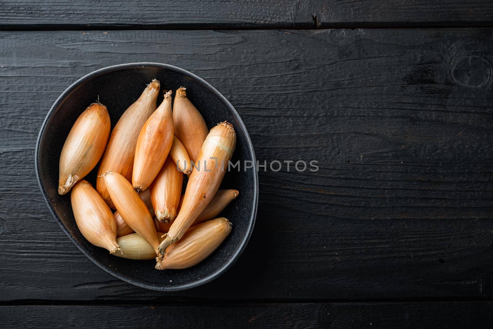 Raw whole baby shallot onion, on black wooden table, flat lay with space for text