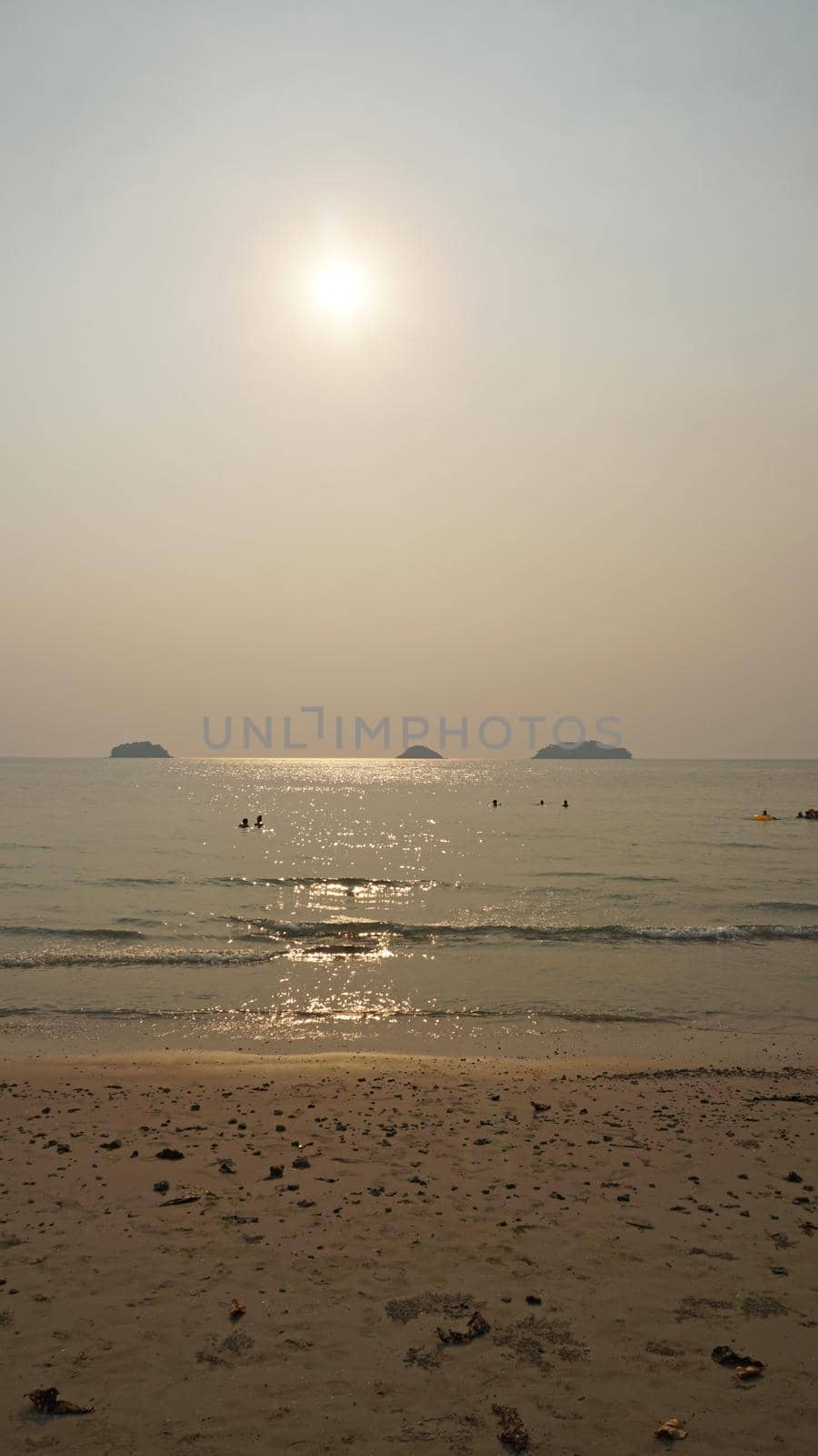 Smog obscures the sun's rays. People relax on the beach. Yellow rays of light. View of the islands, sand, sea and palm trees. Dirty air, smog. Chang Island, Thailand.