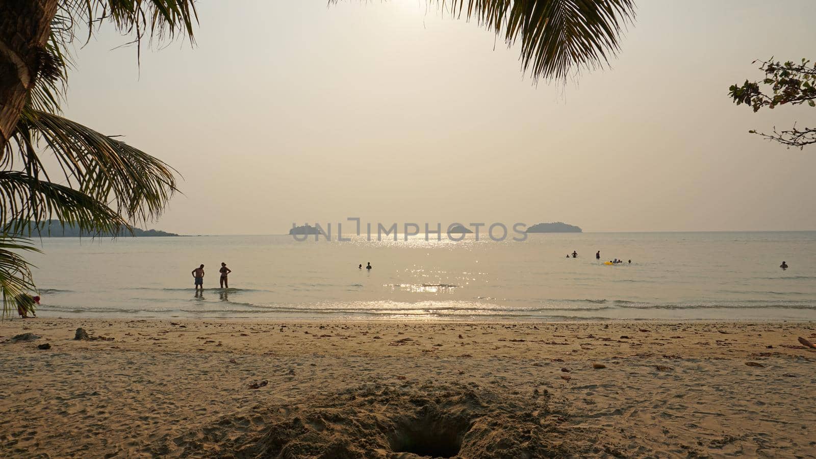 Smog obscures the sun's rays. People relax on the beach. Yellow rays of light. View of the islands, sand, sea and palm trees. Dirty air, smog. Chang Island, Thailand.