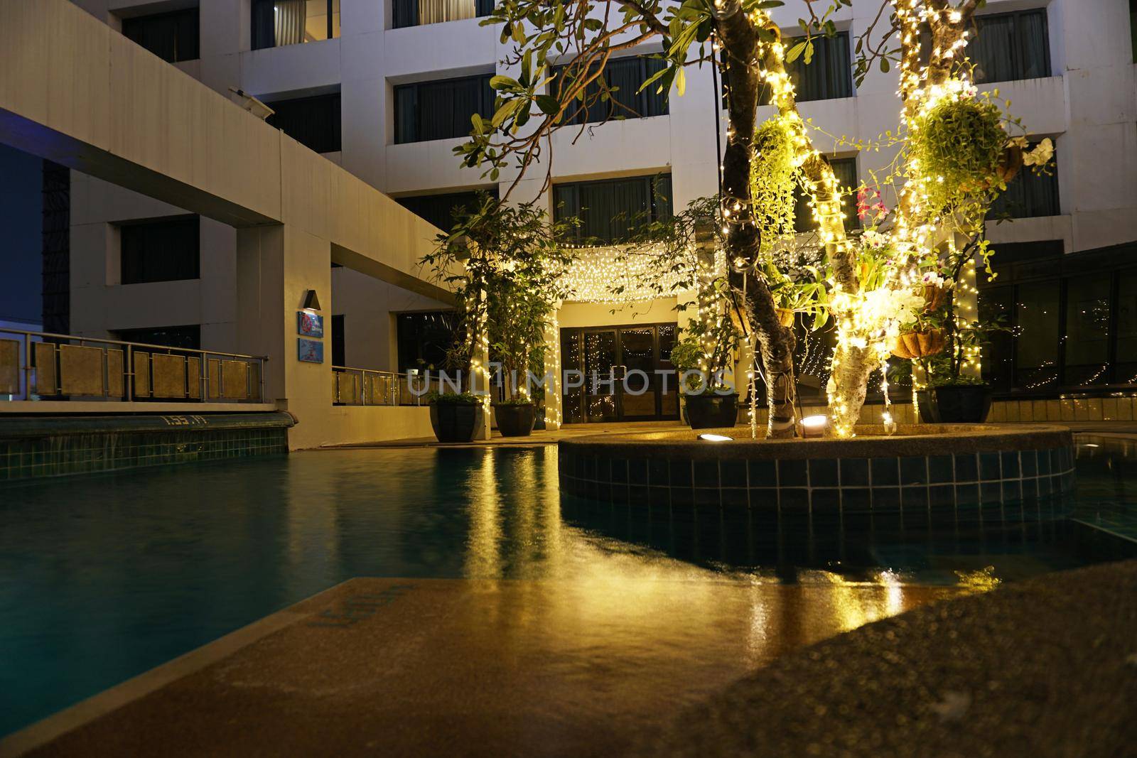 Night pool with beautiful lighting and wood. Romantic mood in hotels. The water reflects the light of the lights that are located on the tree in the middle of the pool and at the entrance. Thailand